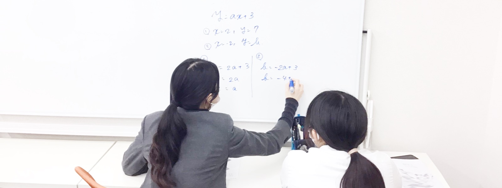ホワイトボードの前で講師が生徒に数学を教えている様子